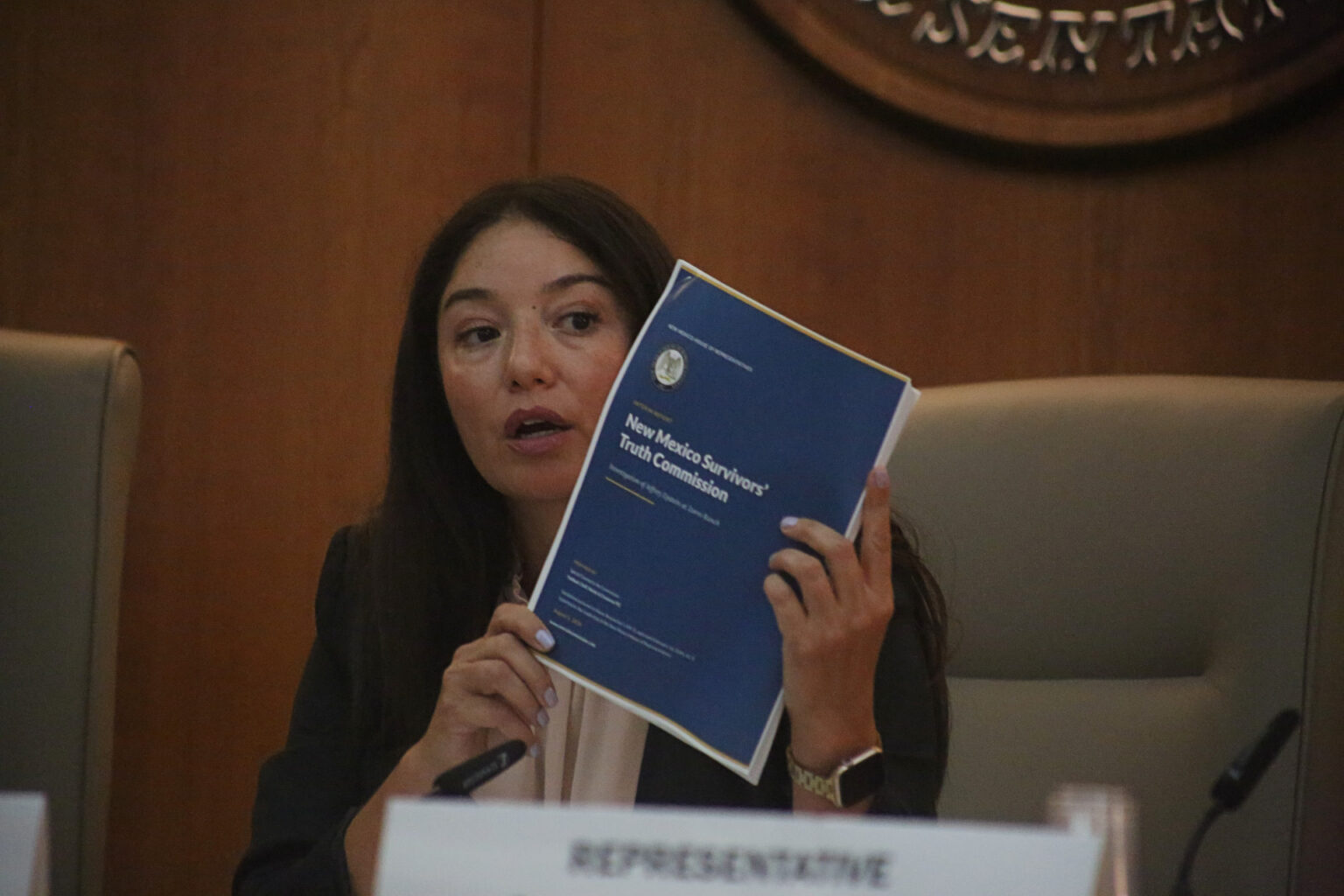 Andrea Romero holds up a blue folder during public meeting.